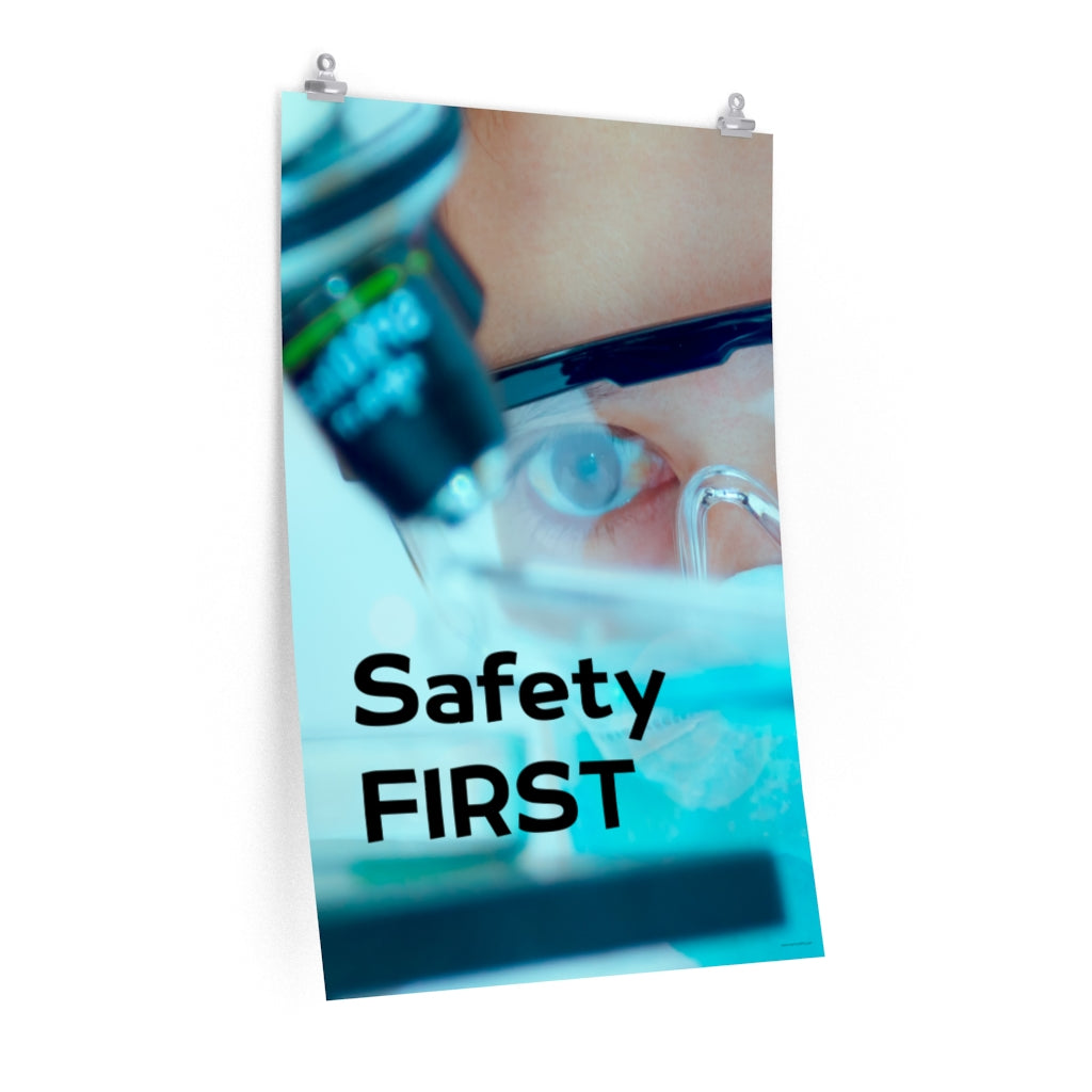 A safety poster showing a close up of a lab worker's eyes examining a sample on a microscope while wearing safety glasses and a mask with the slogan safety first in bold letters.