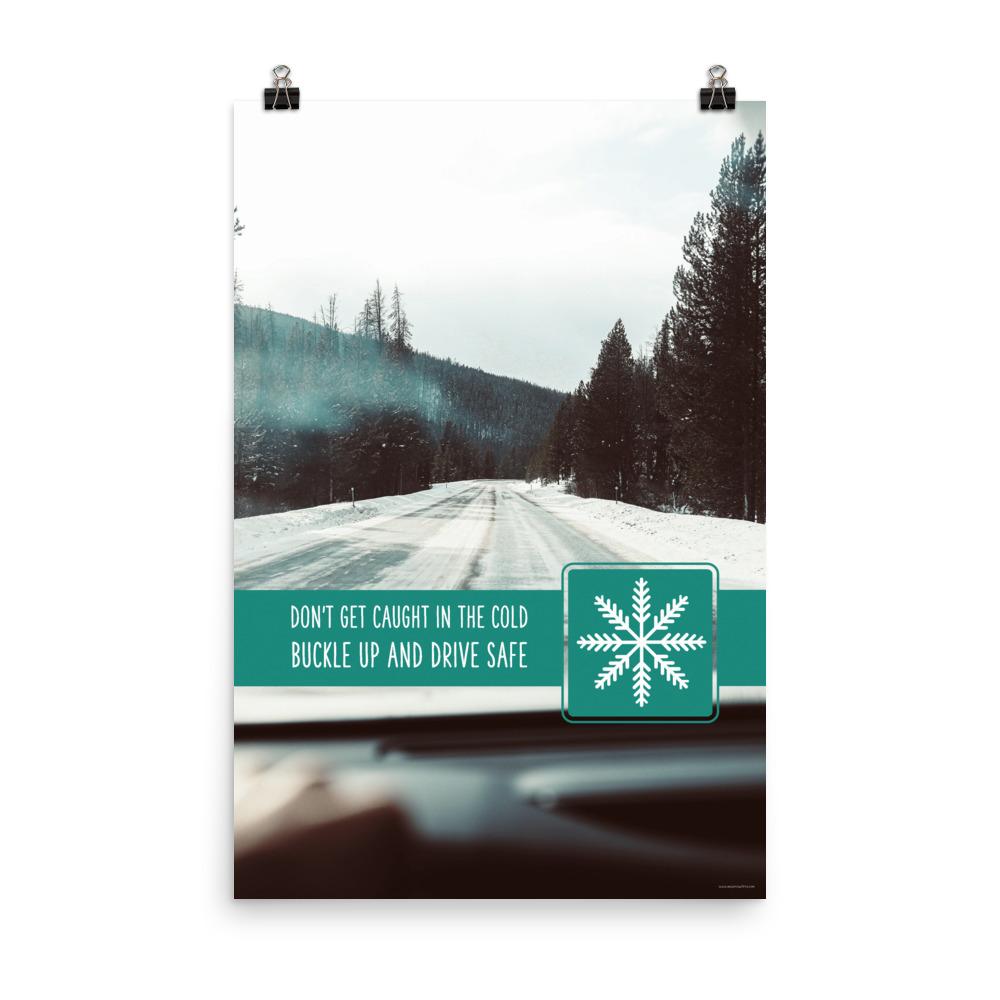 A safety poster showing a picture taken from the dashboard of a car showing an iced over road in the mountains with the slogan don't get caught in the cold, buckle up and stay safe.