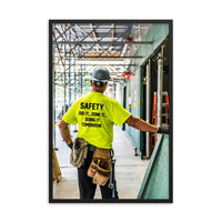 Safety poster showing a construction worker under scaffolding wearing a tool belt, hard hat, safety gloves, and bright yellow shirt with text on the back of his shirt.