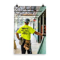 Safety poster showing a construction worker under scaffolding wearing a tool belt, hard hat, safety gloves, and bright yellow shirt with text on the back of his shirt.
