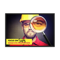 An eye safety poster showing a close up of a man's face wearing safety glasses and a yellow hard hat with a magnifying glass focusing on the right eye with an eye safety slogan underneath him.