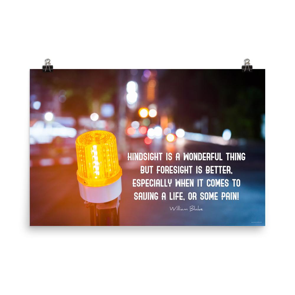 A workplace safety poster depicting a bright orange construction traffic light in the foreground of a blurry nighttime cityscape with a safety quote by William Blake.