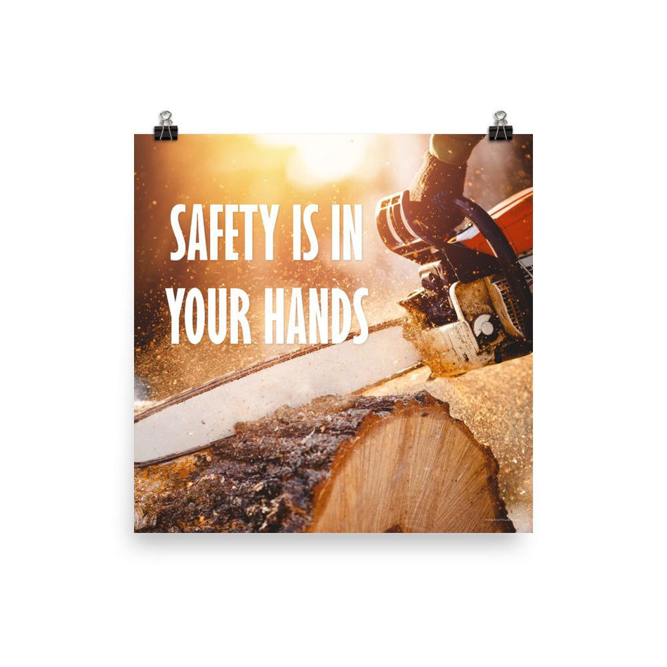 A safety poster showing a close-up of a man's hands holding a chainsaw sawing through a log with sawdust flying everywhere with the text safety is in your hands to the left.