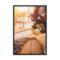 A safety poster showing a close-up of a man's hands holding a chainsaw sawing through a log with sawdust flying everywhere with the text safety is in your hands to the left.