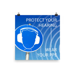A hearing protection poster showing a bright blue construction sign with an illustration of a face wearing ear muffs with sound waves coming from the right and a safety slogan in the upper right and bottom right corners.