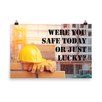 A workplace safety poster showing a yellow hard hat and some gloves sitting on a brick wall on a construction site with the slogan were you safe today, or just lucky written in black stencil font.