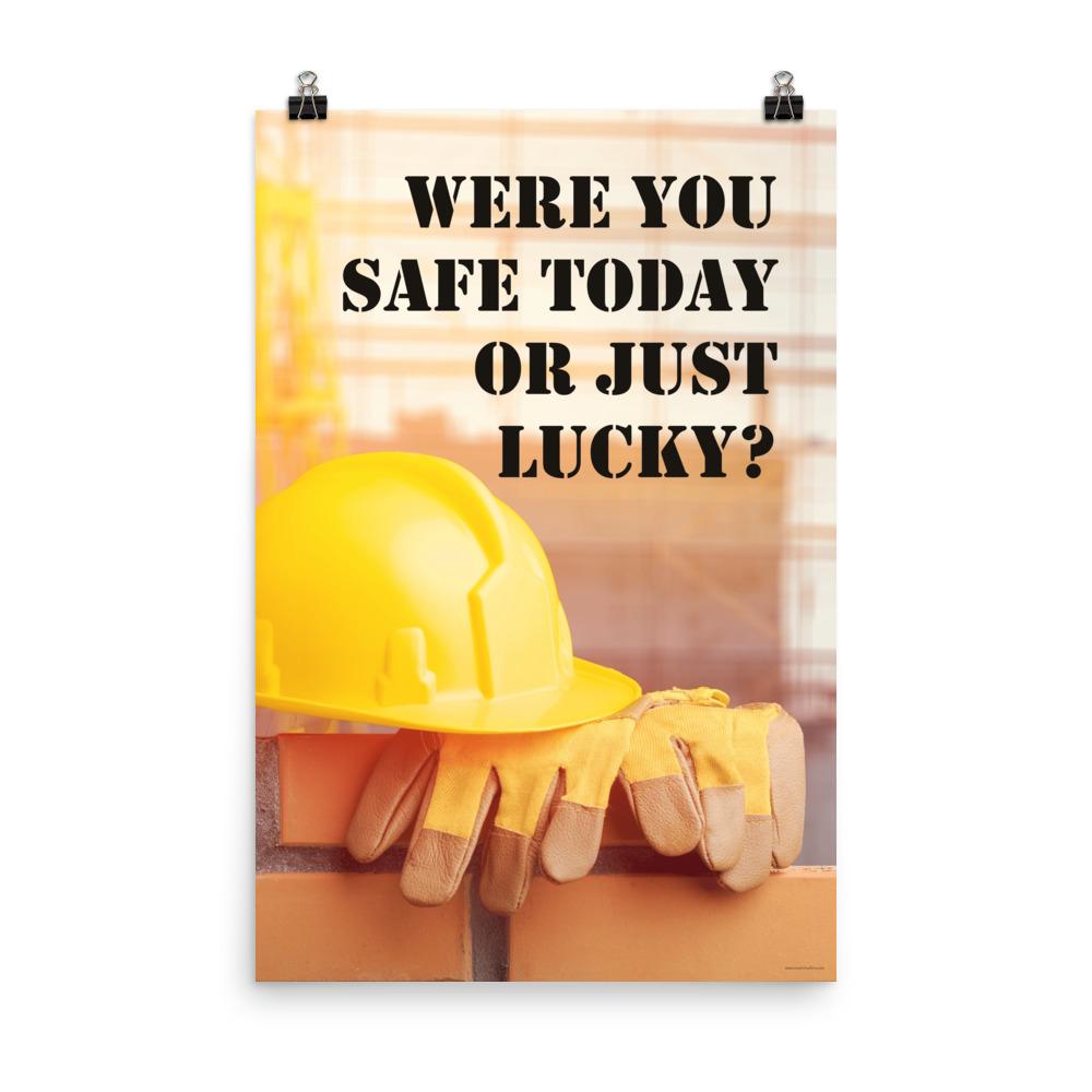 A workplace safety poster showing a yellow hard hat and some gloves sitting on a brick wall on a construction site with the slogan were you safe today, or just lucky written in black stencil font.