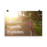 A safety poster showing a little girl riding her bike down a road on a sunny day with the slogan safety isn't expensive, it's priceless.