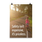 A safety poster showing a little girl riding her bike down a road on a sunny day with the slogan safety isn't expensive, it's priceless.