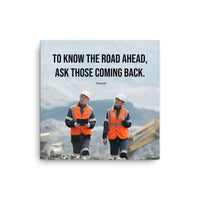 A safety poster showing two workers in reflective vests collaborating on a construction site with the proverb to know the road ahead ask those coming back.
