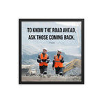 A safety poster showing two workers in reflective vests collaborating on a construction site with the proverb to know the road ahead ask those coming back.