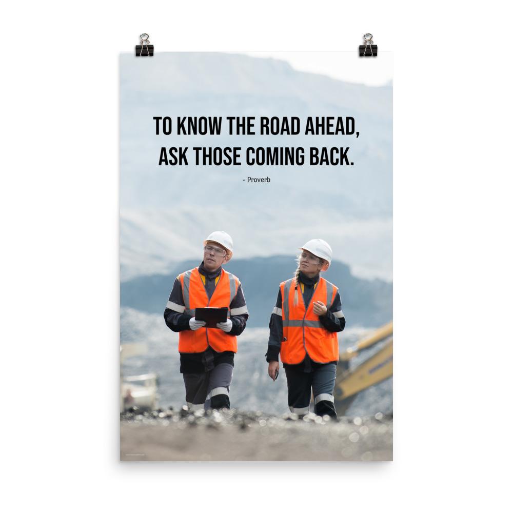 A safety poster showing two workers in reflective vests collaborating on a construction site with the proverb to know the road ahead ask those coming back.