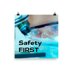 A safety poster showing a close up of a lab worker's eyes examining a sample on a microscope while wearing safety glasses and a mask with the slogan safety first in bold letters.
