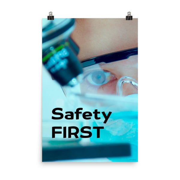 A safety poster showing a close up of a lab worker's eyes examining a sample on a microscope while wearing safety glasses and a mask with the slogan safety first in bold letters.