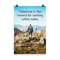 A workplace safety poster showing a man standing on a peak of a mountain with a bright blue sky and mountains behind him with the slogan tomorrow is the reward for working safely today.