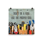 A workplace safety poster showing various tools such as a screwdriver, wrench, and pliers on a wooden table with the slogan don't be a fool use the proper tool.