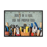 A workplace safety poster showing various tools such as a screwdriver, wrench, and pliers on a wooden table with the slogan don't be a fool use the proper tool.