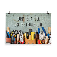 A workplace safety poster showing various tools such as a screwdriver, wrench, and pliers on a wooden table with the slogan don't be a fool use the proper tool.