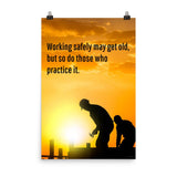 A workplace safety poster showing a construction site and construction workers being silhouetted by a bright and beautiful sunset of different shades of orange with the slogan working safely may get old, but so do those who practice it.