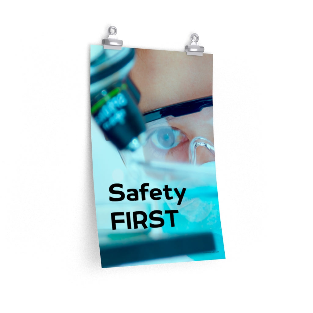 A safety poster showing a close up of a lab worker's eyes examining a sample on a microscope while wearing safety glasses and a mask with the slogan safety first in bold letters.