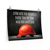 A workplace safety poster showing a bright red hard hat with an ominous black background with the slogan living with your mistakes is harder than you think, wear your safety gear.