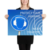 A hearing protection poster showing a bright blue construction sign with an illustration of a face wearing ear muffs with sound waves coming from the right and a safety slogan in the upper right and bottom right corners.