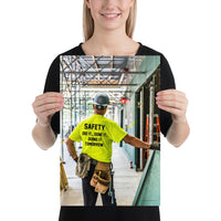 Safety poster showing a construction worker under scaffolding wearing a tool belt, hard hat, safety gloves, and bright yellow shirt with text on the back of his shirt.
