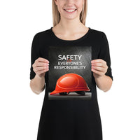 A workplace safety poster showing a red hard hat in front of a grey, industrial-looking background with the slogan safety is everyone's responsibility.