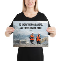A safety poster showing two workers in reflective vests collaborating on a construction site with the proverb to know the road ahead ask those coming back.