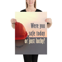 A workplace safety poster showing a red hard hat sitting on a grey wall with a dreamy sunset background and the slogan were you safe today, or just lucky?