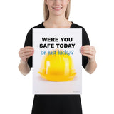 A workplace safety poster showing a yellow hard hat on a plain white background with the slogan were you safe today, or just lucky?