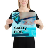 A safety poster showing a close up of a lab worker's eyes examining a sample on a microscope while wearing safety glasses and a mask with the slogan safety first in bold letters.