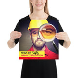 An eye safety poster showing a close up of a man's face wearing safety glasses and a yellow hard hat with a magnifying glass focusing on the right eye with an eye safety slogan underneath him.
