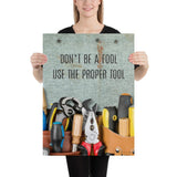 A workplace safety poster showing various tools such as a screwdriver, wrench, and pliers on a wooden table with the slogan don't be a fool use the proper tool.