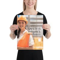 A workplace safety poster showing a young warehouse worker in a yellow hardhat and orange reflective vest holding a clipboard and smiling with the slogan safety is everyone's responsibility.