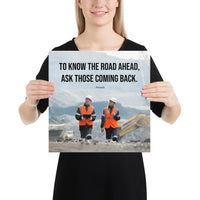 A safety poster showing two workers in reflective vests collaborating on a construction site with the proverb to know the road ahead ask those coming back.