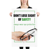 An eye safety slogan showing a close up of a hand presenting out safety glasses with a safety slogan in blue text above.