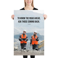 A safety poster showing two workers in reflective vests collaborating on a construction site with the proverb to know the road ahead ask those coming back.