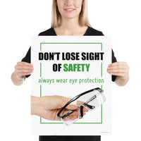 An eye safety slogan showing a close up of a hand presenting out safety glasses with a safety slogan in blue text above.