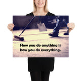 Safety poster showing a closeup of the ground where a warehouse or construction worker is sweeping the workshop floor and an encouraging safety slogan written in bold text.