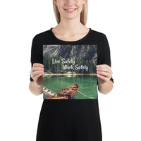 A workplace safety poster depicting a beautiful landscape of mountains in the background of a lake with a little wooden boat in the lake with text saying live safely work safely.