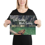 A workplace safety poster depicting a beautiful landscape of mountains in the background of a lake with a little wooden boat in the lake with text saying live safely work safely.