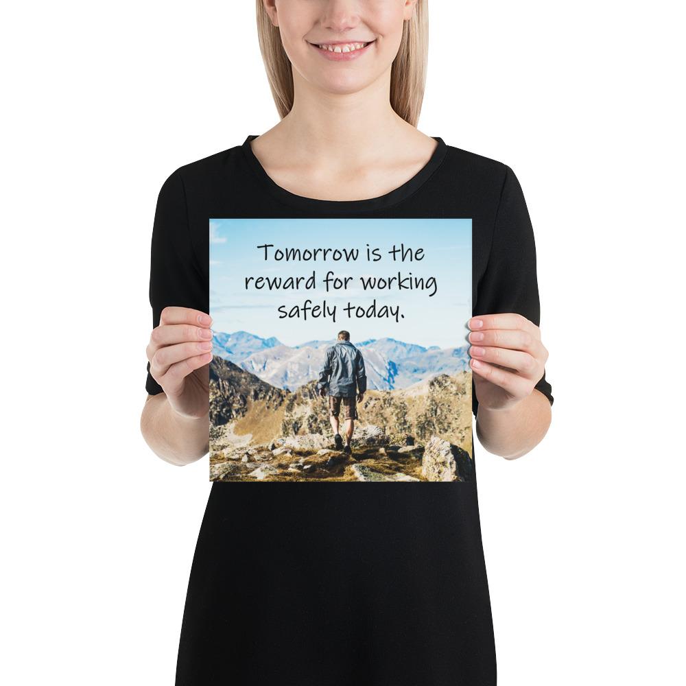 A workplace safety poster showing a man standing on a peak of a mountain with a bright blue sky and mountains behind him with the slogan tomorrow is the reward for working safely today.