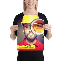 An eye safety poster showing a close up of a man's face wearing safety glasses and a yellow hard hat with a magnifying glass focusing on the right eye with an eye safety slogan underneath him.