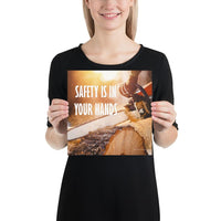 A safety poster showing a close-up of a man's hands holding a chainsaw sawing through a log with sawdust flying everywhere with the text safety is in your hands to the left.