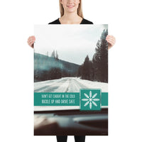 A safety poster showing a picture taken from the dashboard of a car showing an iced over road in the mountains with the slogan don't get caught in the cold, buckle up and stay safe.