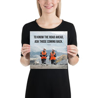 A safety poster showing two workers in reflective vests collaborating on a construction site with the proverb to know the road ahead ask those coming back.
