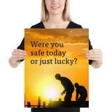 A workplace safety poster showing workers on a construction site being silhouetted in black with a sunset of orange hues in the background with the slogan were you safe today, or just lucky?