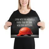 A workplace safety poster showing a bright red hard hat with an ominous black background with the slogan living with your mistakes is harder than you think, wear your safety gear.