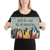 A workplace safety poster showing various tools such as a screwdriver, wrench, and pliers on a wooden table with the slogan don't be a fool use the proper tool.